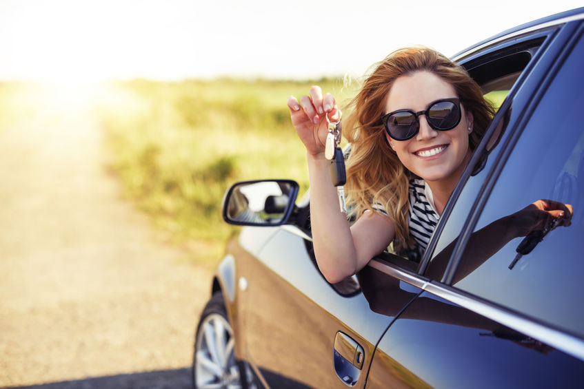 Woman leaning out a car window smiling and holding keys